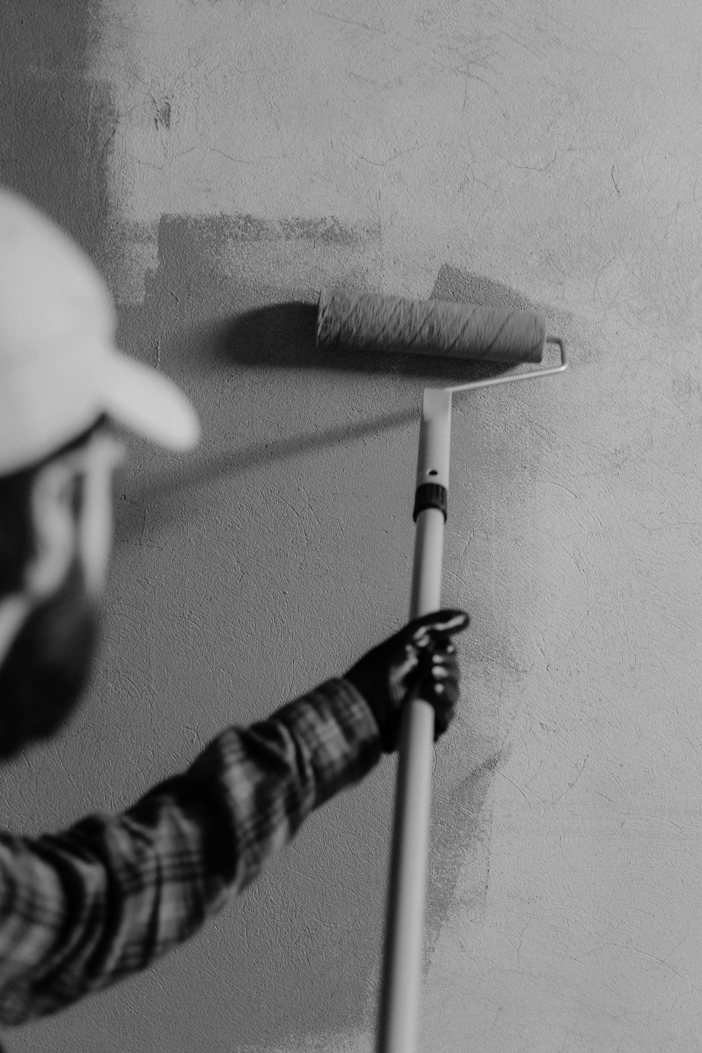 Black and white image of a painter using a roller on an interior wall.