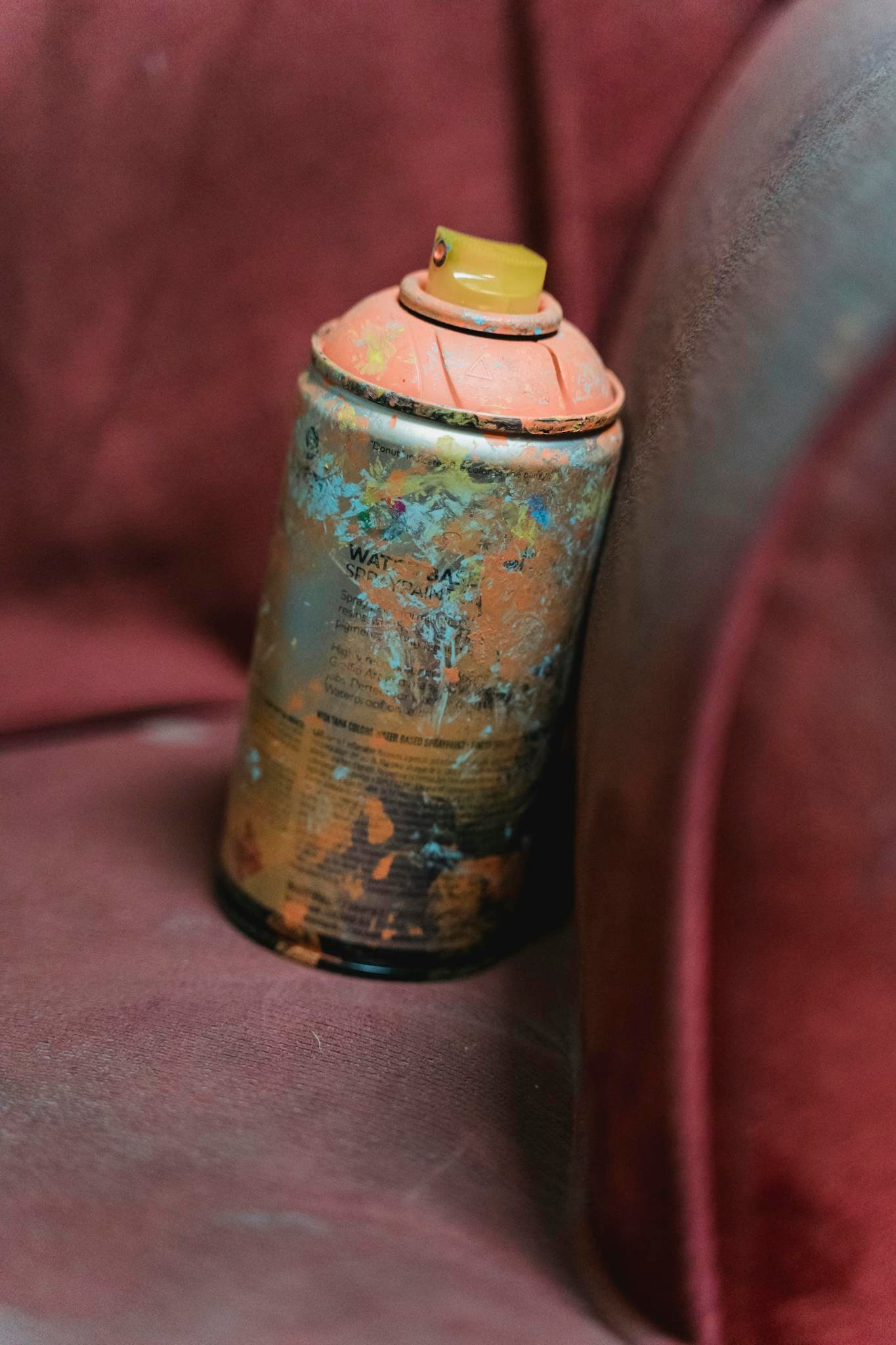 Vintage spray can with peeling paint on a red fabric chair, evoking a rustic and urban feel.